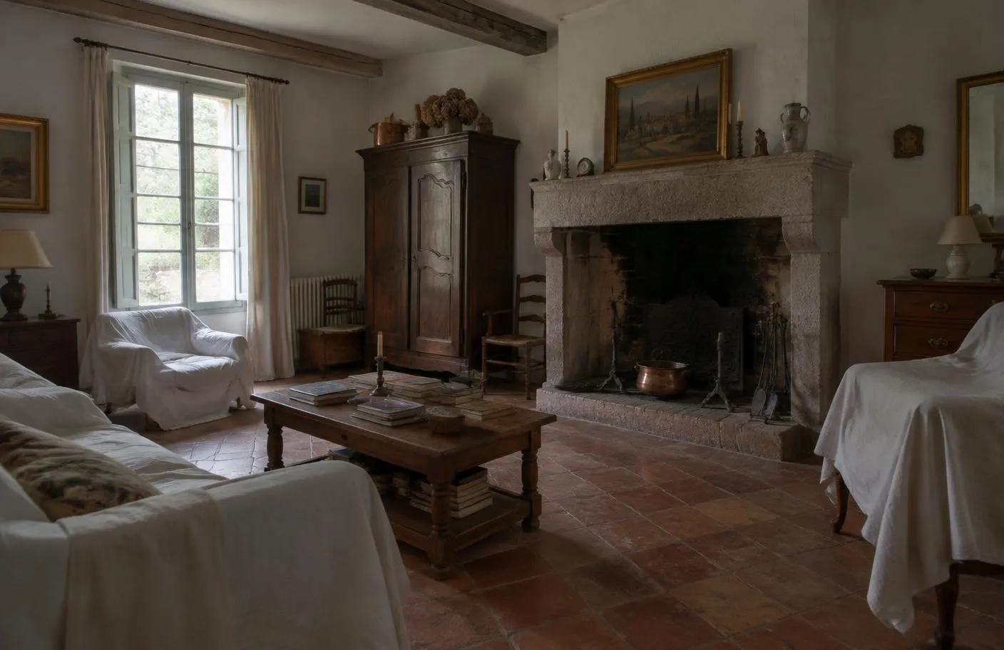 Séjour d'une maison de famille provençale, meubles anciens sous des draps, cheminée en pierre et tomettes