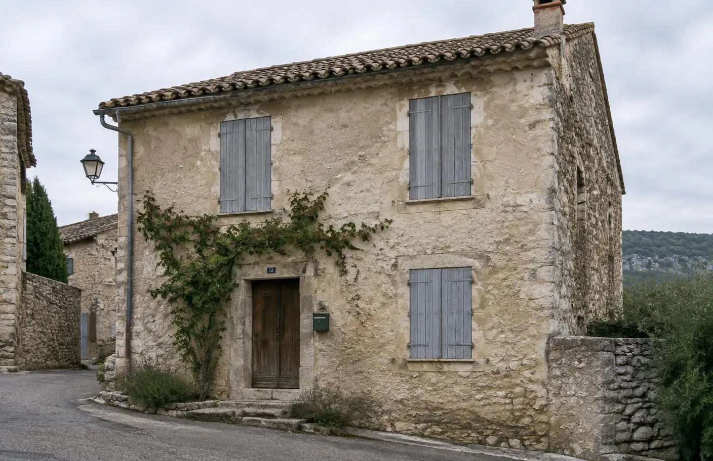 Maison de village en pierre aux volets gris, façade enduite et vigne grimpante, dans une ruelle de Provence