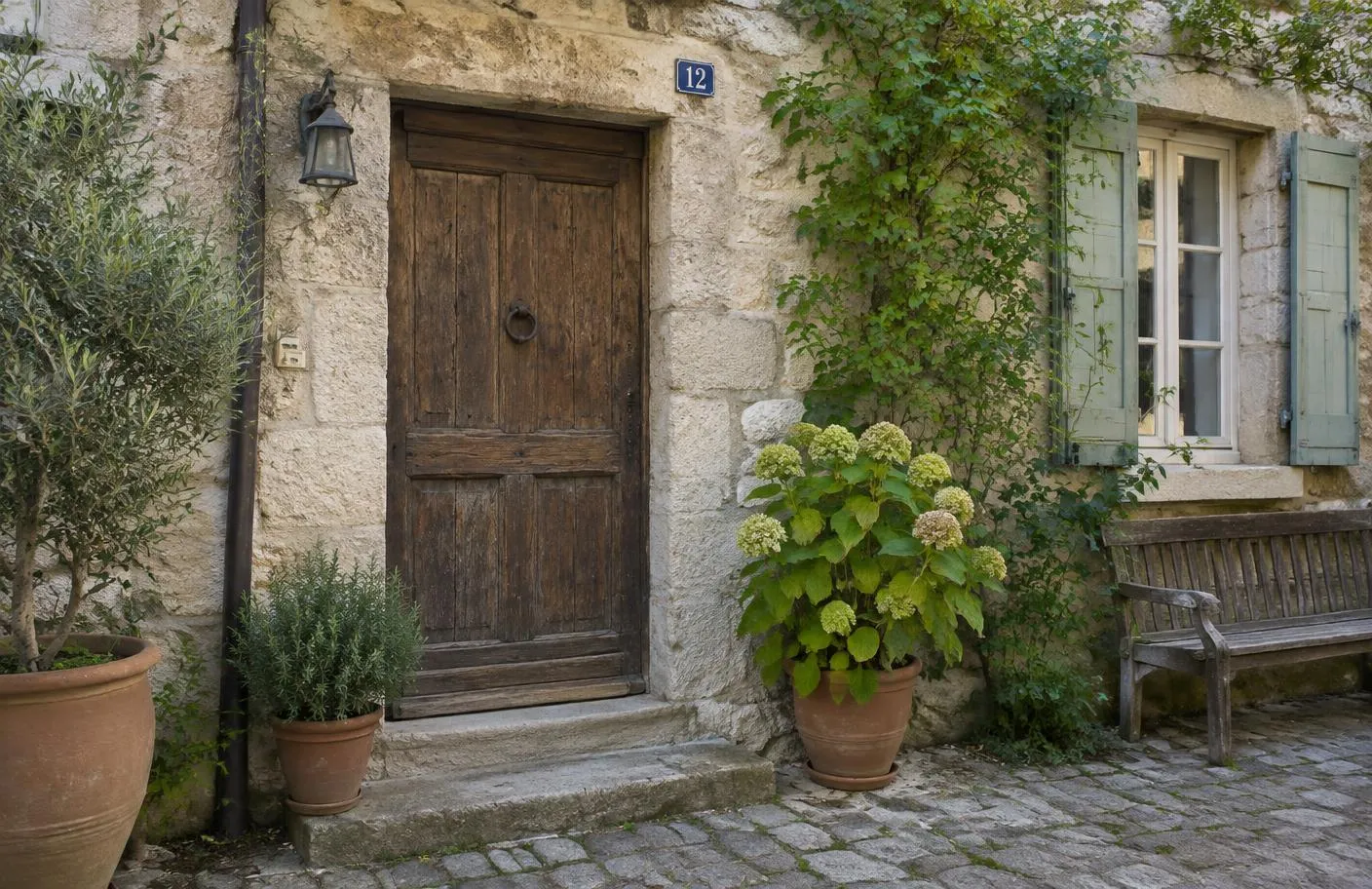 Porte en bois ancienne d'une maison en pierre, pots de fleurs et banc sur une ruelle pavée